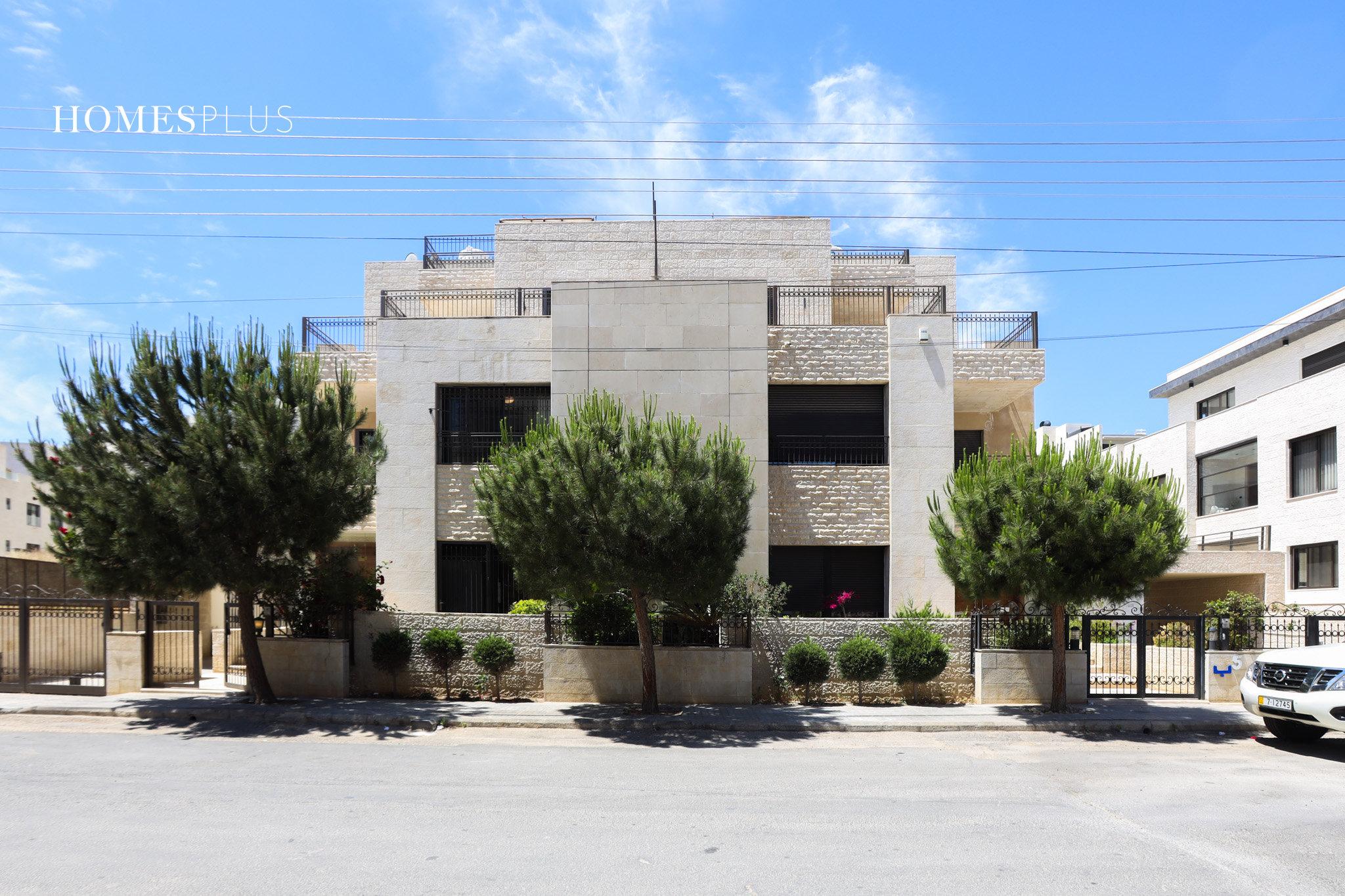 Stone villa behind trees on a street in Abdoun, Amman