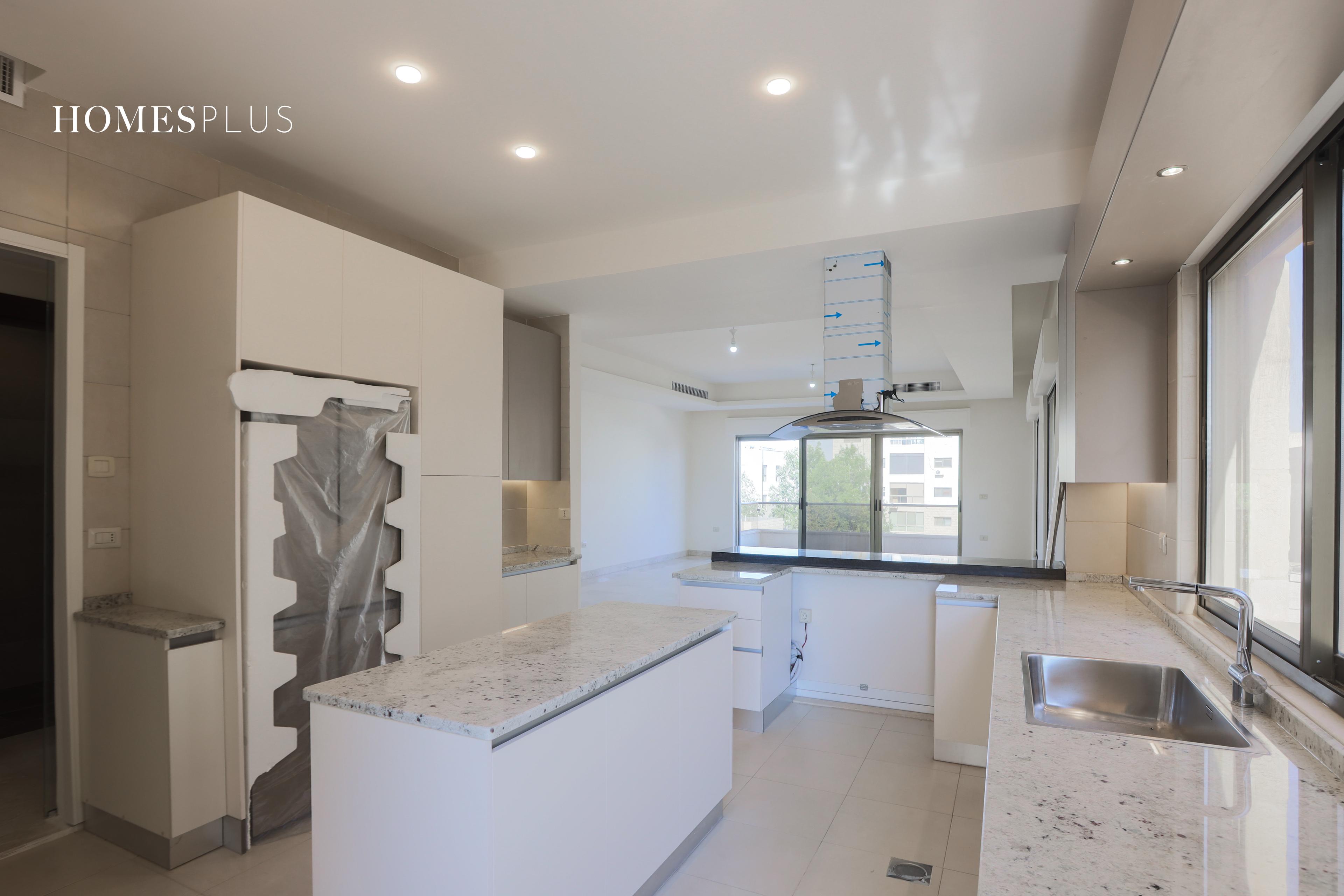 White kitchen with an island in an apartment in Abdoun, Amman